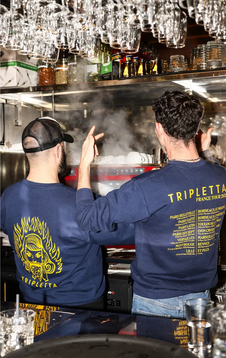 Deux cuisiniers en discussion dans une cuisine Rue Forno, portant un t-shirt de la pizzeria.
