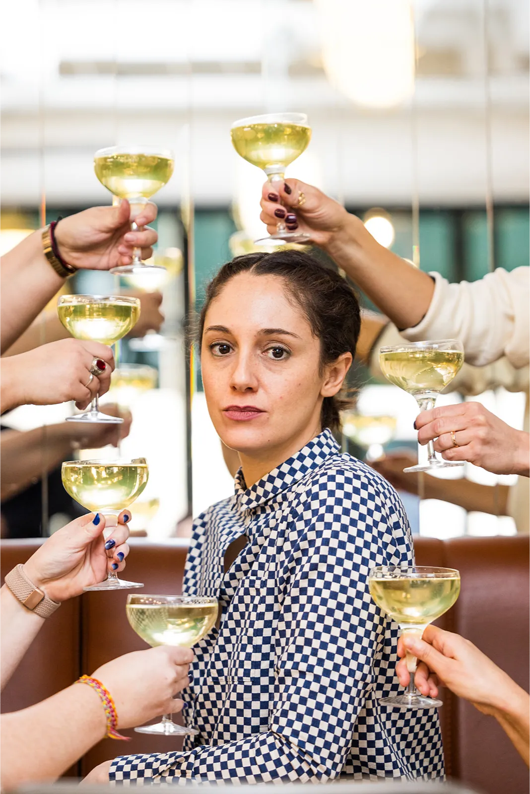 Jeune femme en terrasse d’un restaurant, entourée d’amis trinquant avec plusieurs verres.